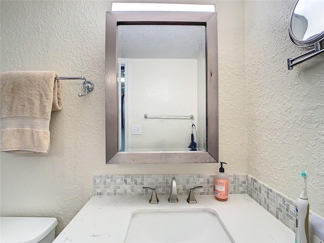 bathroom with vanity, toilet, a textured ceiling, and backsplash