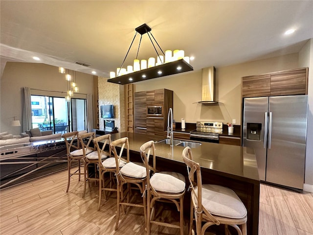 kitchen with a notable chandelier, appliances with stainless steel finishes, sink, wall chimney range hood, and a breakfast bar area