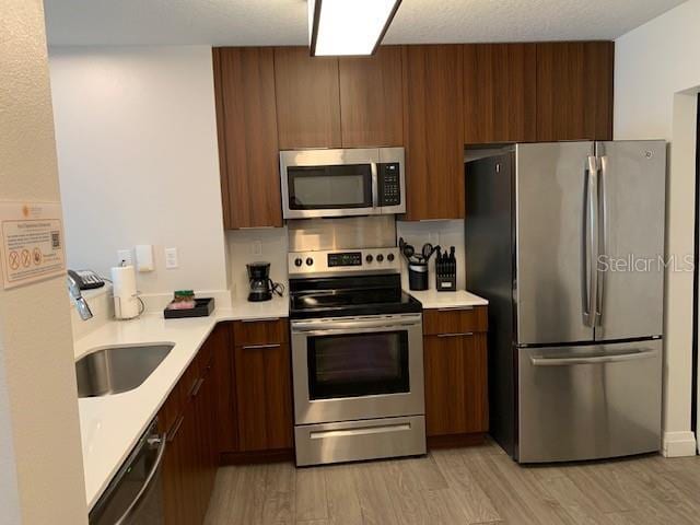 kitchen featuring stainless steel appliances, light countertops, light wood-style flooring, a sink, and modern cabinets