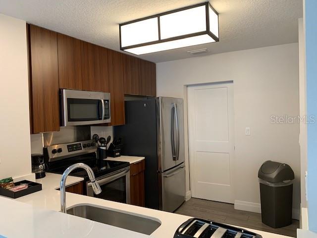 kitchen featuring a textured ceiling, stainless steel appliances, light countertops, and brown cabinets