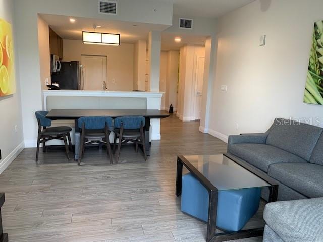 living area featuring light wood-type flooring, visible vents, and baseboards