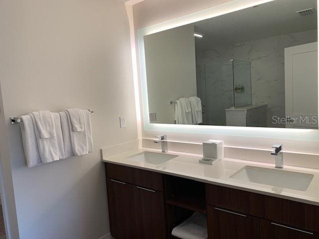 bathroom featuring double vanity, a marble finish shower, and a sink