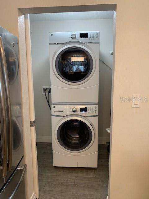 laundry room with stacked washer / drying machine, dark wood-style flooring, baseboards, and laundry area