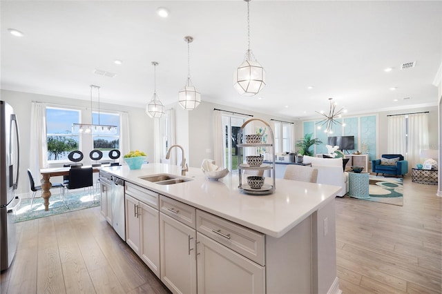 kitchen with sink, an island with sink, light wood-type flooring, white cabinets, and pendant lighting