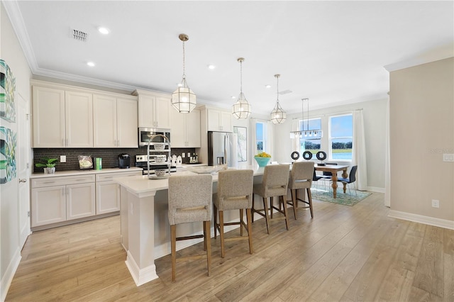 kitchen featuring an island with sink, pendant lighting, light hardwood / wood-style floors, tasteful backsplash, and appliances with stainless steel finishes