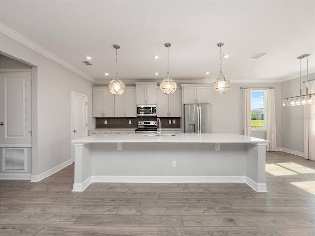 kitchen with pendant lighting, appliances with stainless steel finishes, a breakfast bar, a center island with sink, and tasteful backsplash