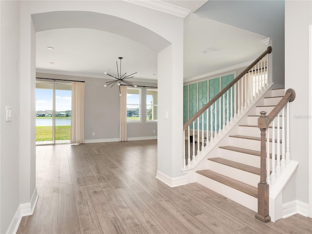 stairway with plenty of natural light, crown molding, light hardwood / wood-style floors, and a water view