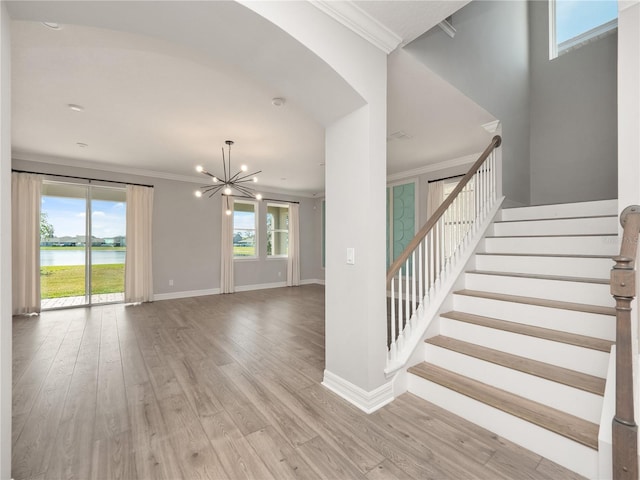 stairway with a water view, light hardwood / wood-style floors, a notable chandelier, and crown molding