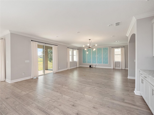 unfurnished living room featuring crown molding, an inviting chandelier, a healthy amount of sunlight, and light hardwood / wood-style flooring