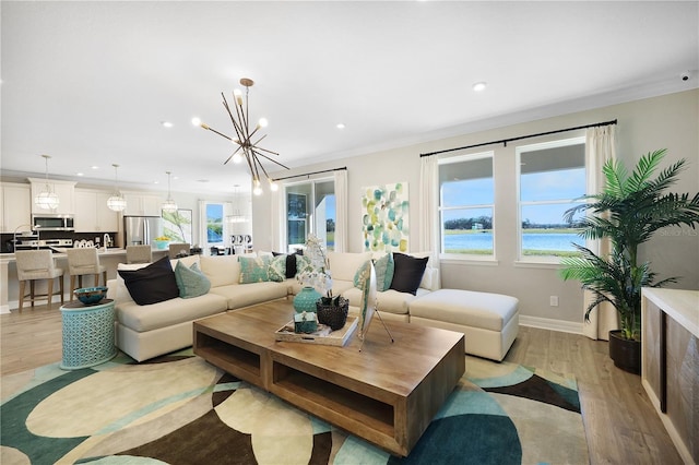 living room with a water view, a notable chandelier, light wood-type flooring, and crown molding