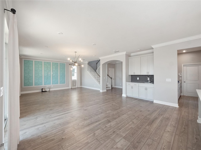 unfurnished living room with an inviting chandelier, crown molding, light hardwood / wood-style floors, and sink