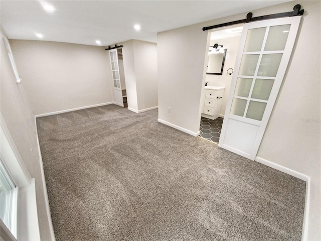 unfurnished bedroom featuring a barn door, sink, dark colored carpet, and ensuite bathroom