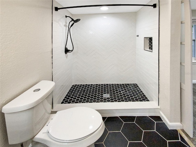 bathroom with tile floors, toilet, and tiled shower