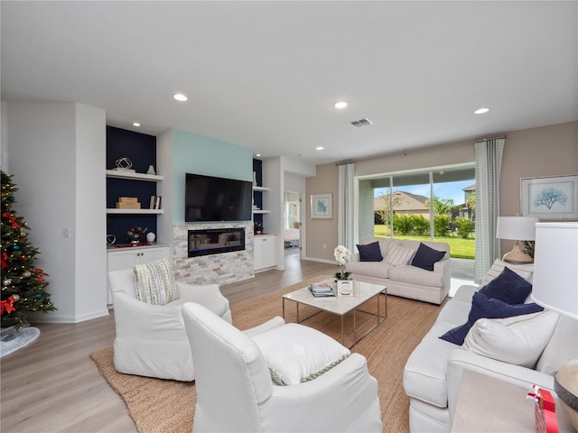 living room featuring built in features, a stone fireplace, and light hardwood / wood-style flooring