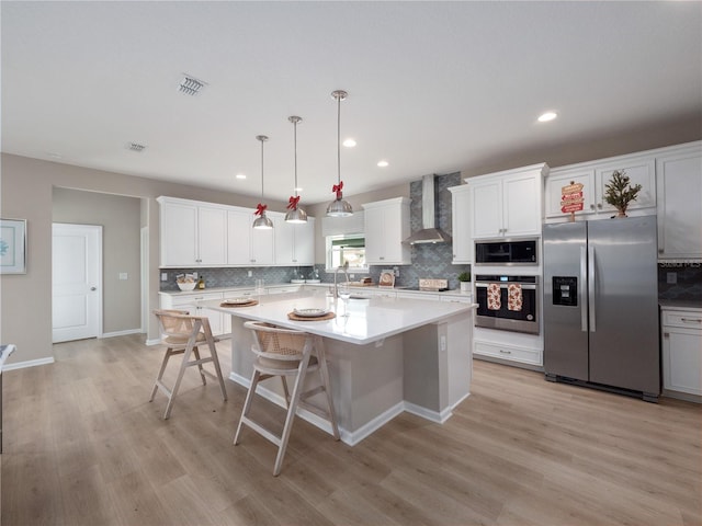 kitchen featuring a center island with sink, light hardwood / wood-style flooring, appliances with stainless steel finishes, and wall chimney range hood