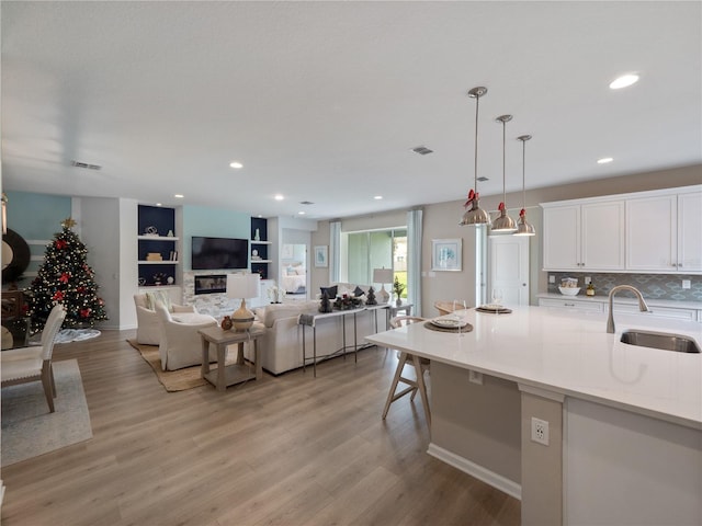 kitchen with sink, light wood-type flooring, built in features, white cabinets, and pendant lighting