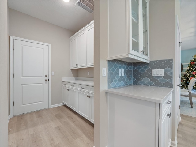 kitchen with white cabinets, backsplash, light wood-type flooring, and light stone counters