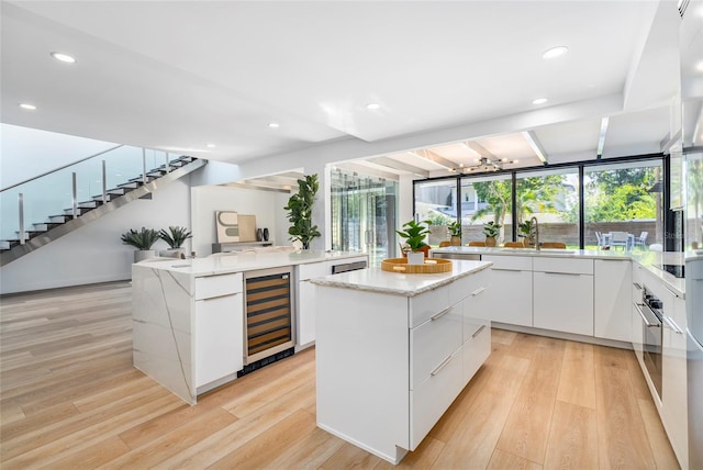 kitchen featuring white cabinets, light hardwood / wood-style flooring, a kitchen island, light stone counters, and beverage cooler