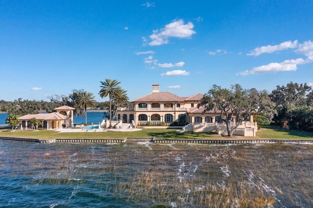 rear view of property with a balcony, a lawn, and a water view