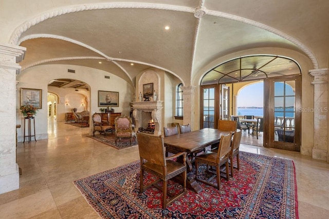 dining area featuring a water view, light tile floors, vaulted ceiling, ornate columns, and french doors