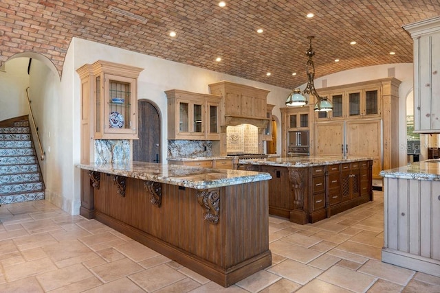 kitchen featuring a kitchen bar, a kitchen island, brick ceiling, and light stone counters