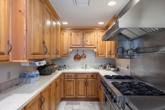 kitchen featuring light tile floors, double oven range, range hood, tile counters, and sink