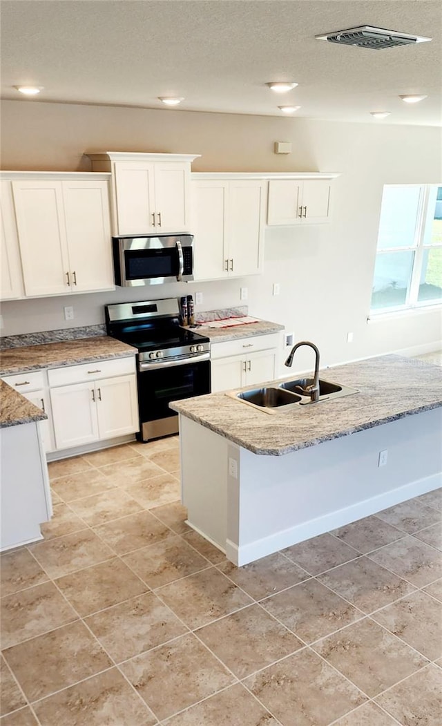 kitchen featuring light stone countertops, white cabinets, appliances with stainless steel finishes, sink, and a kitchen island with sink