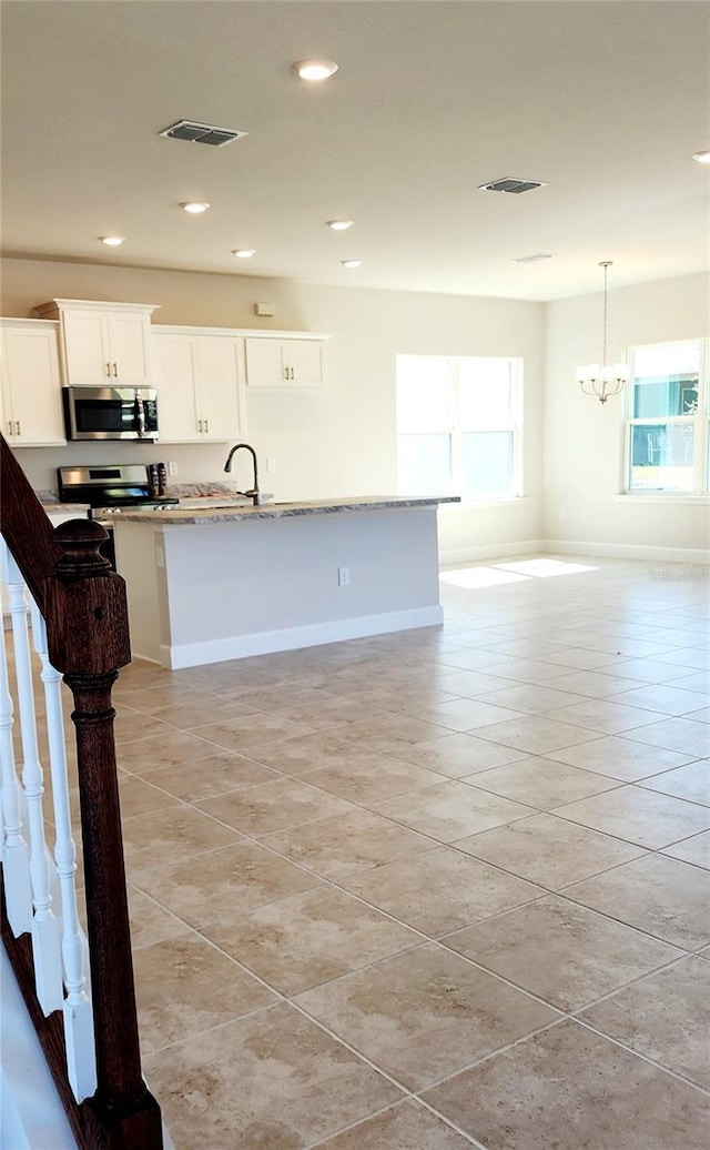 kitchen with light tile patterned floors, white cabinets, a center island with sink, and stainless steel appliances