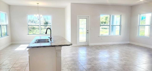 kitchen with hanging light fixtures, sink, light tile patterned floors, a kitchen island with sink, and a notable chandelier