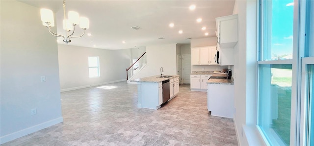 kitchen with appliances with stainless steel finishes, white cabinetry, light stone counters, a notable chandelier, and a center island with sink