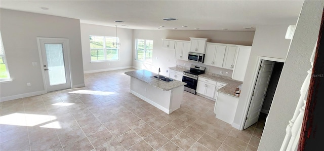 kitchen with appliances with stainless steel finishes, sink, white cabinets, light stone counters, and a kitchen island with sink