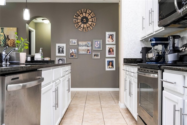 kitchen with stainless steel appliances, light tile flooring, white cabinetry, backsplash, and hanging light fixtures