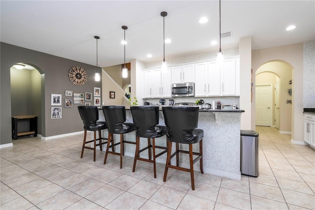 kitchen featuring decorative light fixtures, light tile flooring, white cabinetry, and a breakfast bar