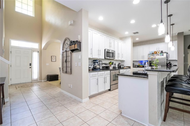 kitchen featuring a kitchen breakfast bar, white cabinets, appliances with stainless steel finishes, tasteful backsplash, and decorative light fixtures