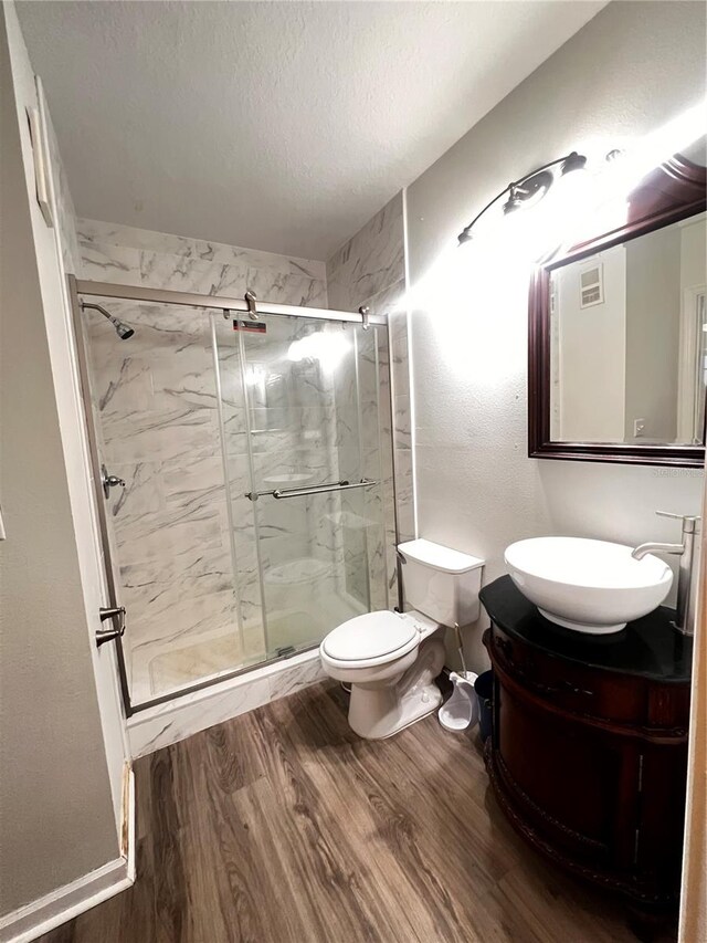 bathroom with vanity, wood finished floors, visible vents, a marble finish shower, and a textured ceiling