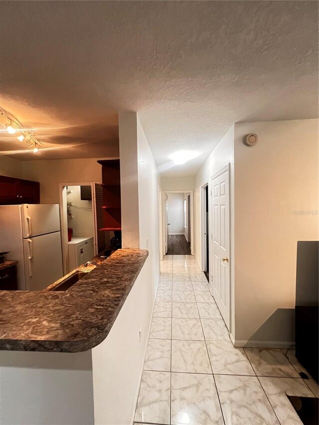 kitchen featuring freestanding refrigerator, a sink, a textured ceiling, dark countertops, and marble finish floor