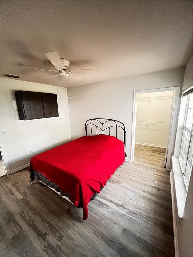 bedroom featuring visible vents, a walk in closet, ceiling fan, wood finished floors, and a closet