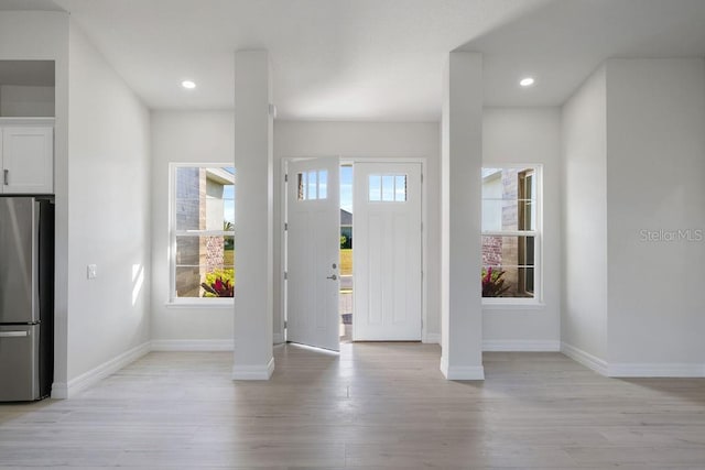 foyer featuring decorative columns, a healthy amount of sunlight, and light hardwood / wood-style floors