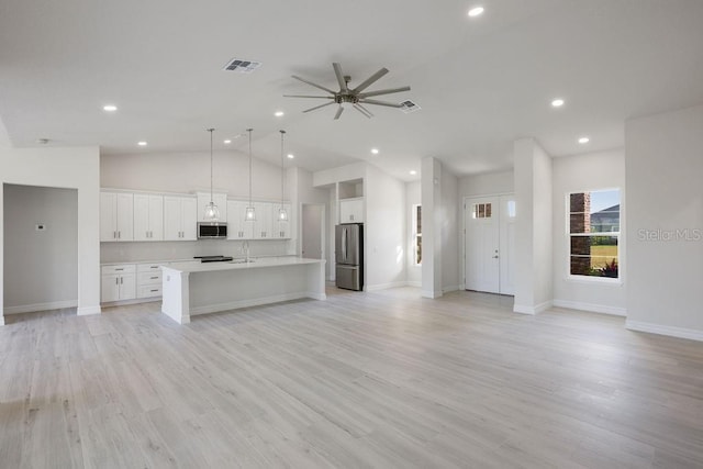 kitchen with sink, hanging light fixtures, stainless steel appliances, white cabinets, and a center island with sink