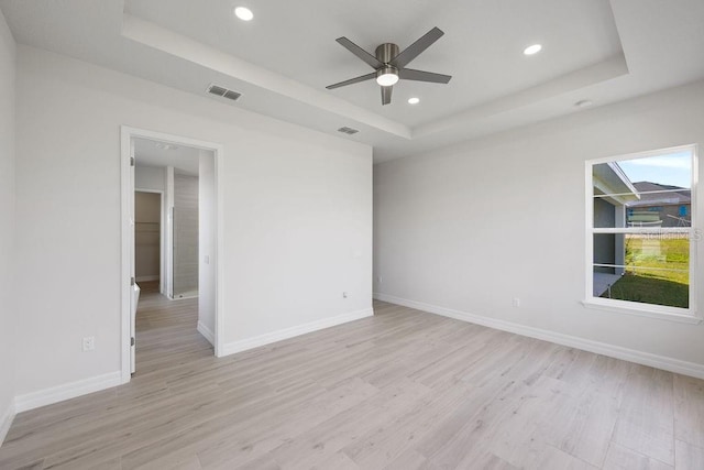 spare room with a tray ceiling, light hardwood / wood-style flooring, and ceiling fan