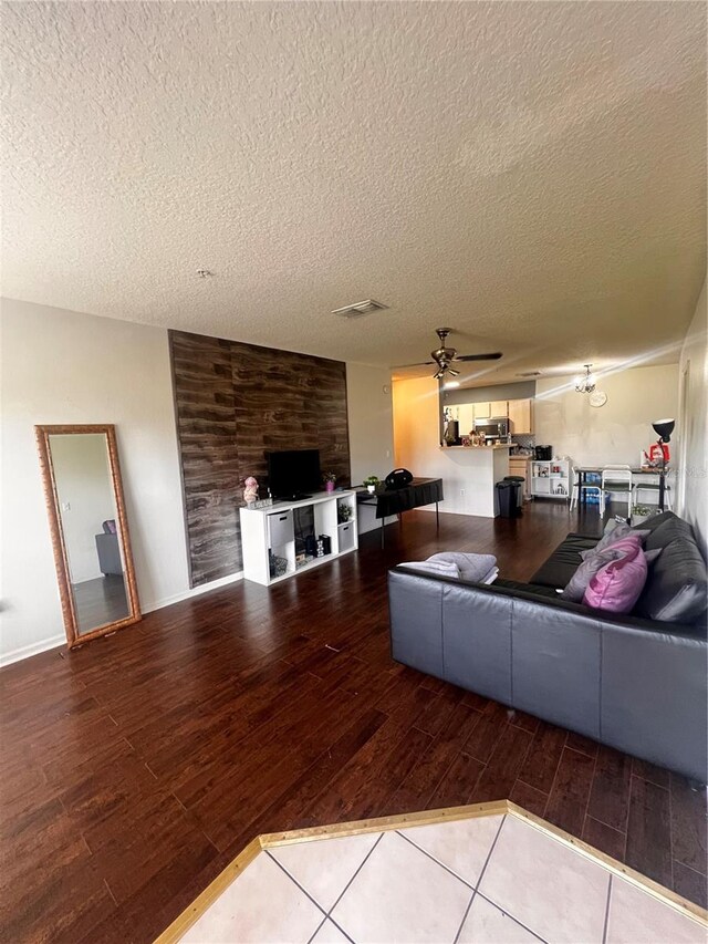 tiled living room featuring wood walls, a textured ceiling, and ceiling fan