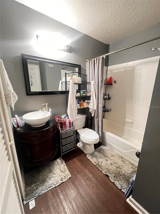 full bathroom featuring toilet, shower / bath combination with curtain, a textured ceiling, large vanity, and hardwood / wood-style flooring