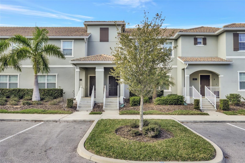 townhome / multi-family property featuring a tile roof, uncovered parking, and stucco siding