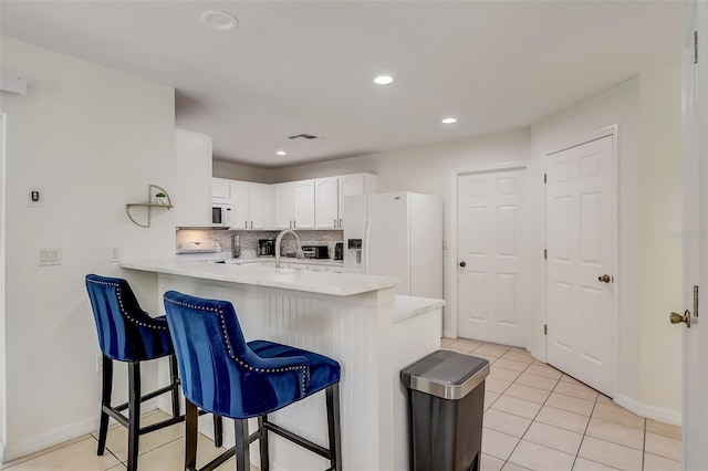 kitchen with a kitchen breakfast bar, light tile floors, tasteful backsplash, white appliances, and white cabinets