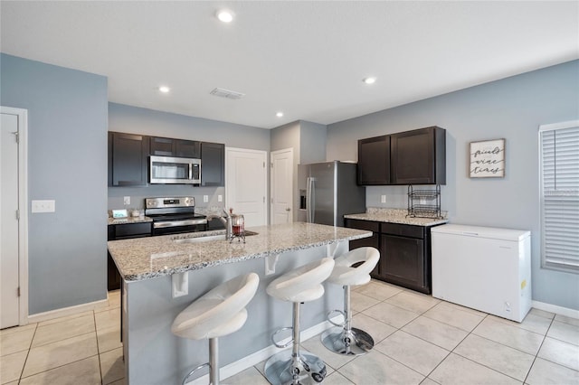 kitchen featuring dark brown cabinetry, sink, a center island with sink, light tile patterned floors, and appliances with stainless steel finishes