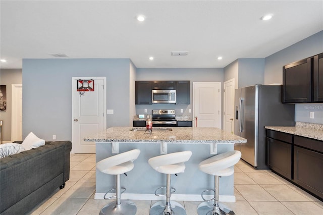 kitchen featuring light stone countertops, an island with sink, light tile patterned floors, and appliances with stainless steel finishes