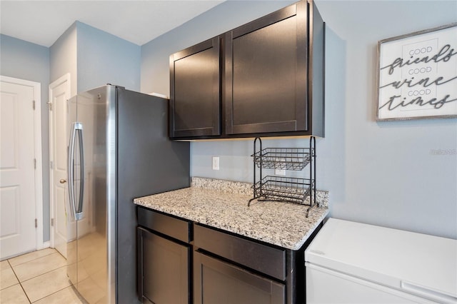 kitchen featuring light stone countertops, light tile patterned floors, dark brown cabinetry, and stainless steel refrigerator