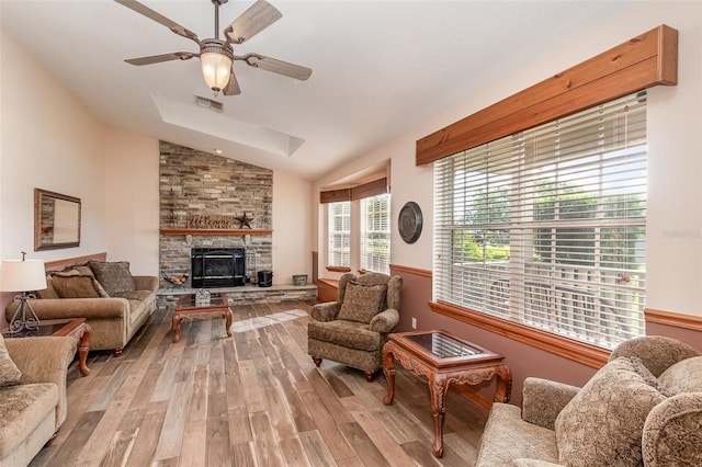 living room with lofted ceiling, light hardwood / wood-style floors, a stone fireplace, and ceiling fan