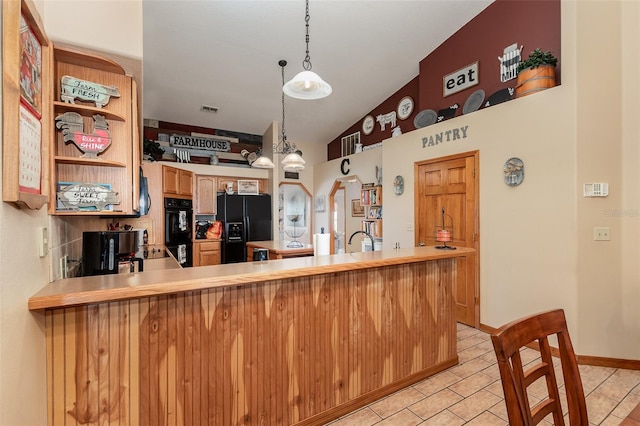 kitchen featuring pendant lighting, light tile floors, kitchen peninsula, black appliances, and lofted ceiling