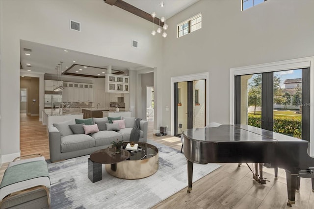 living room with a notable chandelier, sink, light wood-type flooring, a towering ceiling, and french doors